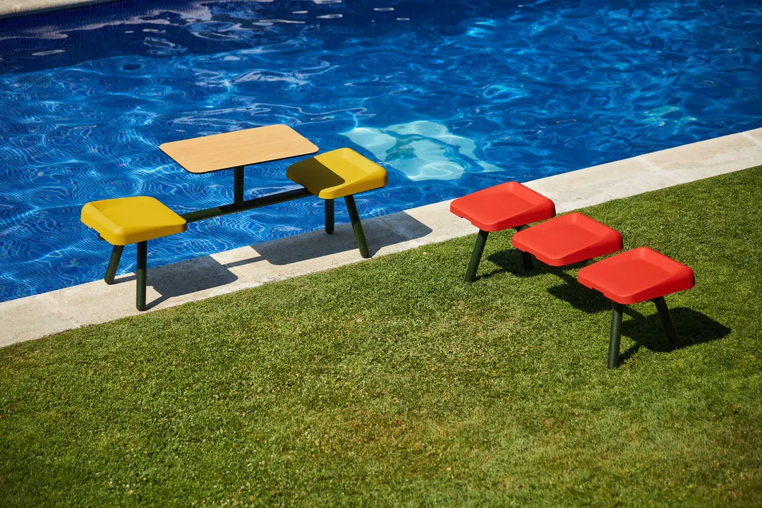 Bancos Slim rojos y conjunto con mesa amarillo sobre el césped junto a una piscina