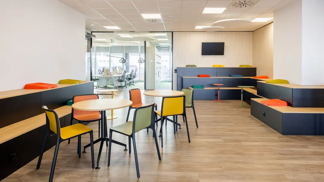 Zona de reunión de oficina con gradas de madera y cojines Slim de colores